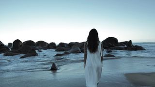 Woman walking on beach towards boulders