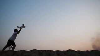 Boy Running In A Field And Playing With A Toy Wooden Airplane In His Hands At Sunset