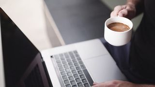 A person drinking coffee while using a laptop