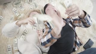 Top view of rich couple on rug laying in money