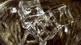 Macro Shot of Pouring Whiskey into Glass with Ice Cubes