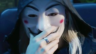 Hacker in a scary mask sitting in front of computer screens