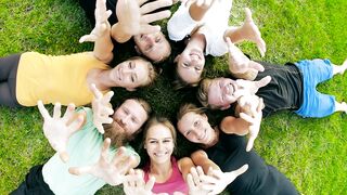Friends lying on the grass waving at the camera