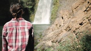Woman standing in front of waterfall on a sunny day