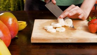 Person cutting banana for a fruit cocktail