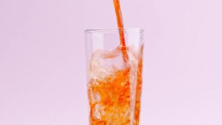 A stream of soda fills up a crystal glass with ice
