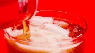 A coke soda can being poured into a glass full of ice