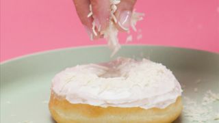 Spreading shredded coconut on a glazed donut