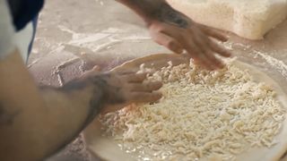 Chef tossing grated cheese on a pizza