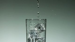 Water drops falling into a glass with ice cubes