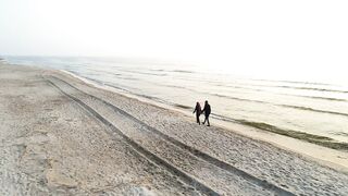 Young couple holding hands walking on beach at sunset