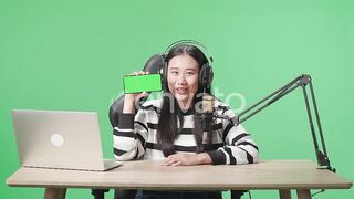 Asian Woman Live Streaming with Green Screen Mobile Phone and Headphones - A Creative and Interactive Visual Experience