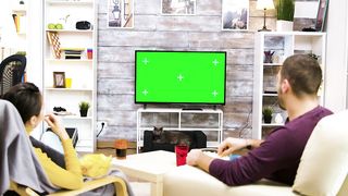 A Cozy Evening In: Couple Watching Green Screen TV and Enjoying Popcorn - A Relatable and Relaxing Scene