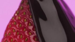 Covering a strawberry with liquid chocolate on a lilac background