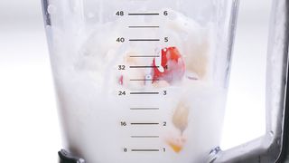 Red and yellow fresh fruit falling into a blender full of milk.