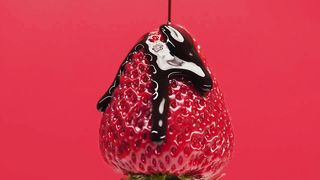 Cover a strawberry with chocolate syrup on a red background.