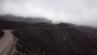An aerial shot captures a secluded mountain road shrouded in mist, evoking a sense of mystery