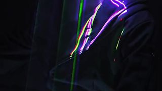 A man sitting beneath laser lights in cyberpunk glasses