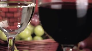 Glasses with red and white wine with a basket of grapes behind