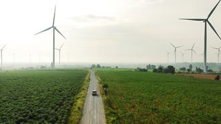 Scenic Drive: Aerial View of Car Cruising Through Wind Turbines and Green Fields