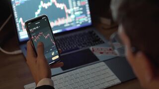 trader performing financial analysis of cryptocurrency using a phone app and laptop