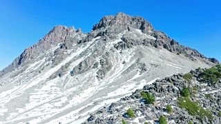 Flying over a monumental rocky mountain with visible snow and small greenery patches