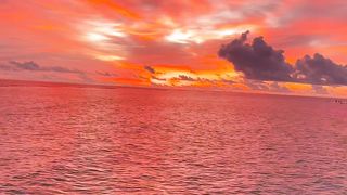 A beautiful sunset in the Maldives fills the sky with shades of crimson, pink and orange, reflected in the warm waters of the Indian Ocean.