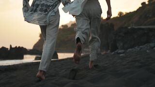 A loving gay couple runs on the beach holding hands at sunset.
