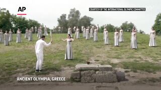 High priestess hands over Olympic flame to first torchbearer at ceremony in Ancient Olympia.