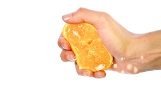 Hand of a person squeezing an orange on a light background