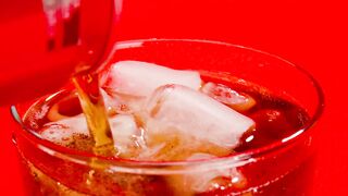 A coke soda can being poured into a glass full of ice