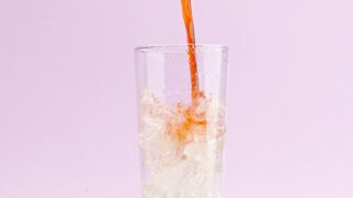 A stream of soda fills up a crystal glass with ice