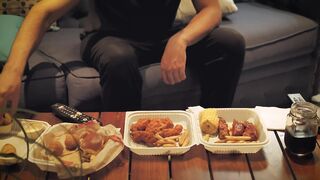 Table in a living room with fast food while a man watches television