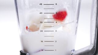 Red and yellow fresh fruit falling into a blender full of milk.