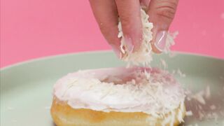 Spreading shredded coconut on a glazed donut
