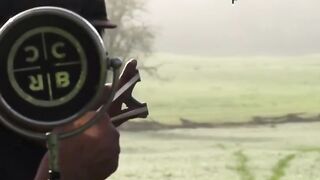 Man strikes a single water droplet with a slingshot, aiming through a mirror.