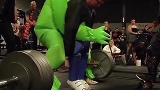 An alien does a barbell lift with a human