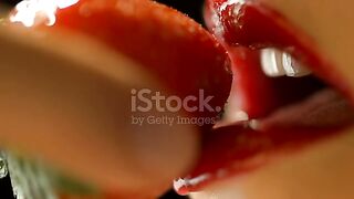 Super Slow Motion Close-Up shot of a young sensual woman with colorful red lips eating a strawberry.