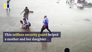 Security guard helps pedestrians knocked off feet in strong winds.