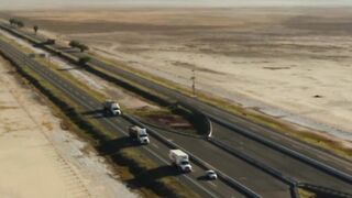 Vehicle traffic with road traverses the plain desert terrain under the scorching sun
