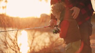 A small child accompanied by his father is spinning his fishing rod.