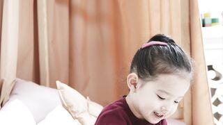 Baby Toys - little girl looking at pictures in a book while sitting on a bed | Trending HD Vide