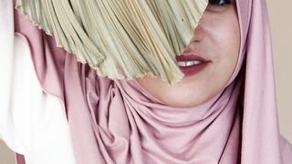 Wonder Woman - woman in pink hijab smiling while covering part of her face with a leaf | Trendi