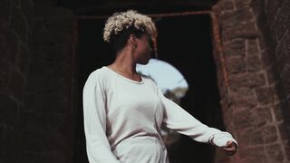 The Shy Snow Woman and the Cursed Ring - a woman with curly hair standing in front of a stone w