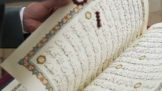 Notes on Being a Man - a man turning pages of quran while praying with prayer beads | Trending