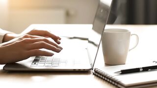 Professional Hands Typing on Laptop with Coffee and Notebook