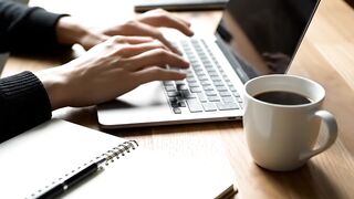 Close-up of Hands Typing on Laptop at Wooden Workspace with Coffee