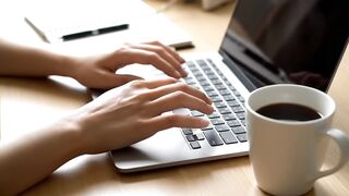 Person Typing on Laptop Keyboard at a Workspace with Coffee