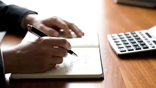 Close-up of Businessman Writing in Notebook with Calculator