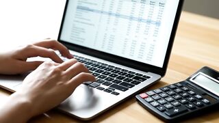 Person Working on Financial Spreadsheet with Laptop and Calculator